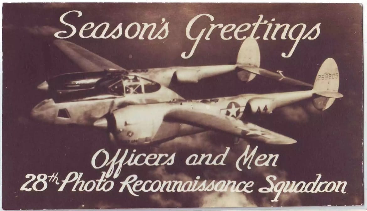 A wartime Season's Greetings card: a P-38 Lightning banks against a dark sky, script text below reads "Officers and Men, 28th Photo Reconnaissance Squadron."