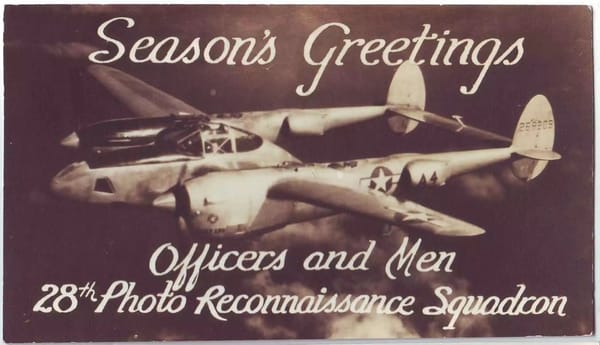 A wartime Season's Greetings card: a P-38 Lightning banks against a dark sky, script text below reads "Officers and Men, 28th Photo Reconnaissance Squadron."